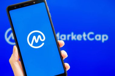 Ukrayna, Odessa - 9 Ekim 2021: Arkaplanda CMC logosu olan akıllı telefon ekranında çalışan CoinMarketCap uygulaması ile el ele tutuşmak. Dünyanın en güvenilir kripto para birimi veri yetkisi