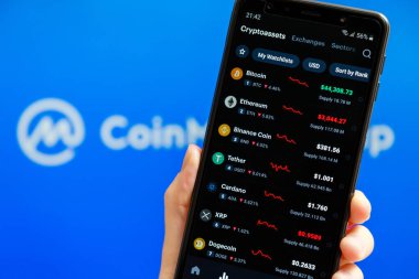 Ukraine, Odessa - October, 9 2021: Hand holding mobile with CoinMarketCap app running at smartphone screen with list of todays cryptocurrency prices, CMC logo at background. Crypto data authority