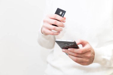 Kyiv, Ukraine - December, 2 2022: Close up of female hands holding Monobank credit card and using smartphone on white background. Woman paying securely online, using banking service. Online shopping.
