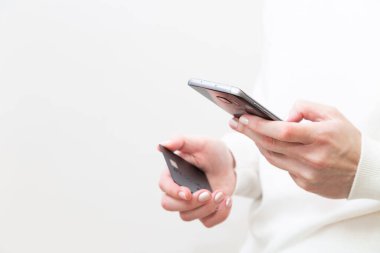 Close up of female hands holding credit card and using smartphone on white background. Woman paying securely online, using banking service, ordering in internet store. Online shopping.