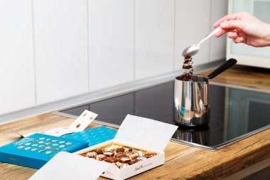 Zurich, Switzerland - January, 7 2023: Lindt Mini Pralines Box. Open small gift box of Swiss chocolate candies and hand of young woman making Turkish coffee at kitchen stove top.
