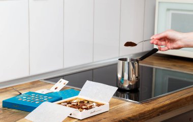 Zurich, Switzerland - January, 7 2023: Lindt Mini Pralines Box. Open small gift box of Swiss chocolate candies and hand of young woman making Turkish coffee at kitchen stove top. clipart