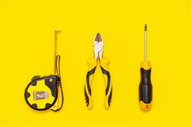 Sarı zemin üzerinde bank aletleri, tornavida, pense ve mezura kesme seti, düz uzanma