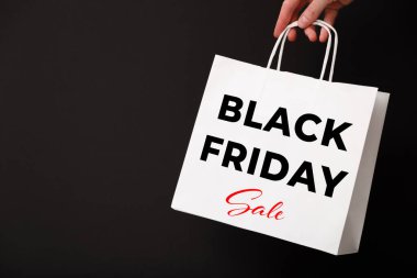 Siyah arka planda Kara Cuma metni olan beyaz alışveriş çantası tutan bir kadın. İndirim, indirim, alışveriş konsepti