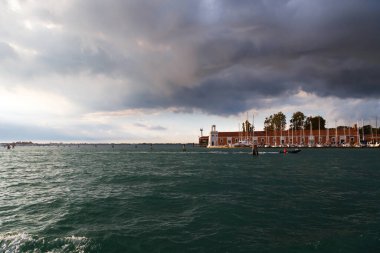 Venedik, San Giorgio Maggiore adasının deniz feneri Faro 'su, arka planda koyu mavi fırtınalı gökyüzü olan yelkenli..