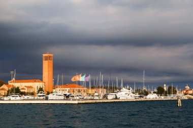İtalya, Venedik 'teki Castello' nun doğu ucundaki Sant 'Elena Kilisesi' nin çan kulesi ve yat limanı. Fırtınalı havada Venedik lagününden arkaplanda kara bulutlu gökyüzü görüntüsü.