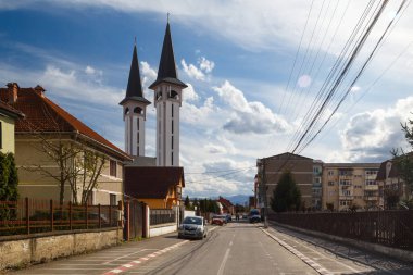 Romanya, Avrig - 26 Nisan 2022: Romanya 'nın Avrig kentinde Ortodoks kilisesine giden tipik bir cadde. Şehir manzarasında iki mimari tarzın karışımı: Romen ve Sovyet. Parlak güneşli bir gün.