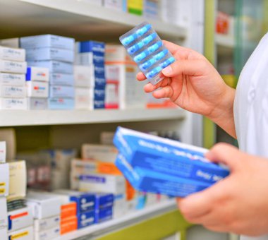 Eczacı eczanede ilaç kutusu ve kapsül paketi tutuyor.