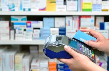 Eczanedeki raflarda bir sürü ilaç var ve alışveriş yapıyorlar, kredi kartıyla ödeme yapıyorlar ve terminali kullanıyorlar.