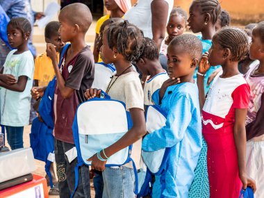 Bour, Senegal - Aralık 2020 civarı. Kimliği belirsiz bir grup genç, güneşli bir yaz gününde okulun bahçesinde ayakta dikiliyorlar. Uluslararası NGO 'nun yeni çantalar almasına sevindim. Zavallı kırsal çocuklar..