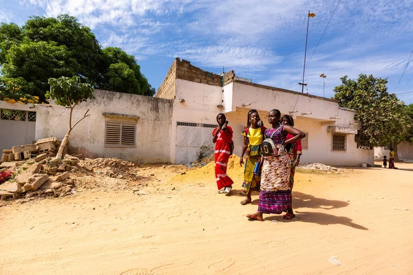 Bour, Senegal - 2021 Temyiz Dairesi. Tanımlanamayan okul çağındaki kızlar ve erkek öğrenciler güneşli bir bahar gününde okuldan sonra fakir köyde geziyorlar. Covid 19 pandemisi sırasında yüz maskesi yok..