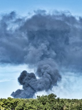 Yanan bir plastik geri dönüşüm yeri, gökyüzü mavi yaz gününde koyu siyah bir duman yığınına neden olur. Tehlike, keder. Terörist saldırı ya da patlama. Çevre felaketi