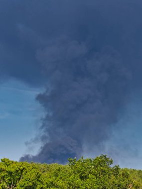 Yanan bir plastik geri dönüşüm yeri, gökyüzü mavi yaz gününde koyu siyah bir duman yığınına neden olur. Tehlike, keder. Terörist saldırı ya da patlama. Çevre felaketi