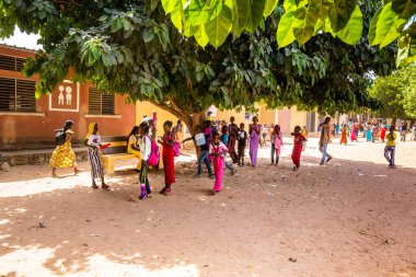 Bour, Senegal - Aralık 2020 civarı. Sınıfın sonundaki çocuk parkında yürüyen kimliği belirsiz Afrikalı öğrenciler. Renkli kıyafetlerle. Kırsal ve yoksul köylerde hayat