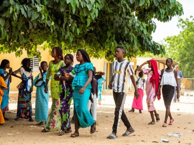 Bour, Senegal - Aralık 2020 civarı. Kimliği belirsiz bir grup genç, güneşli bir yaz gününde okulun bahçesinde ayakta dikiliyorlar. Uluslararası NGO 'nun yeni çantalar almasına sevindim. Zavallı kırsal çocuklar..