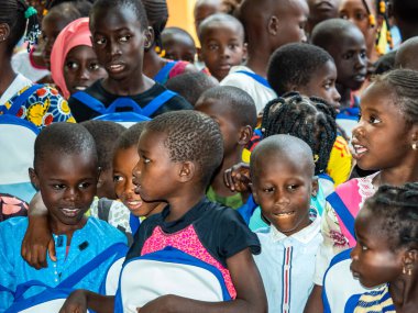 Bour, Senegal - Aralık 2020 civarı. Kimliği belirsiz bir grup genç, güneşli bir yaz gününde okulun bahçesinde ayakta dikiliyorlar. Uluslararası NGO 'nun yeni çantalar almasına sevindim. Zavallı kırsal çocuklar..