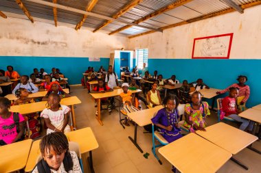 Bour, Senegal - Aralık 2020 civarı. Tanımlanamayan ciddi ve üzgün Afrikalı çocuklar ilkokuldaki bir sınıfta masalarında oturuyorlar. Yeni masaları, çatısı, tabloları olan yeni sınıf. Uluslararası STK yardımları nedeniyle.