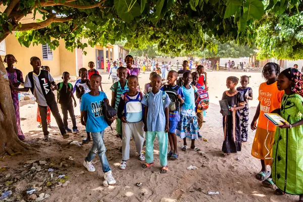 Bour, Senegal - Aralık 2020 civarı. Kimliği belirsiz bir grup genç, güneşli bir yaz gününde okulun bahçesinde ayakta dikiliyorlar. Uluslararası NGO 'nun yeni çantalarını bekliyoruz. Zavallı kırsal çocuklar..