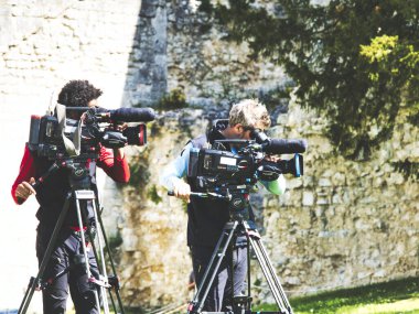 Jumieges, Fransa - Nisan 2019. Profesyonel film için kimliği belirsiz iki kameraman. . Yüksek çözünürlüklü dijital video kamera ön açı görünümü hangi kayıt veya pan tilt shift profesyonel baş tripod üzerinde tv ticari üretim çekim ou