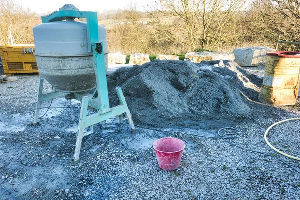 Cement machine close to bunch of gravel stones with red bucket of water. Construction working