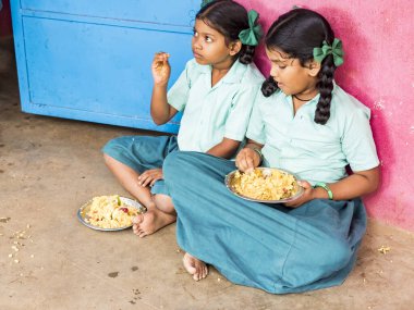Puducherry, Tamil Nadu, Hindistan - Aralık yaklaşık, 2018. Bazı masala ile pirinç onların sağ eli ile yemek tanımlanamayan zavallı sınıf kızlarla yerde açık havada üzerinde oturan üniformalar. Öğle yemeği zamanı, genel hükümet okulda sağlıksız gıda