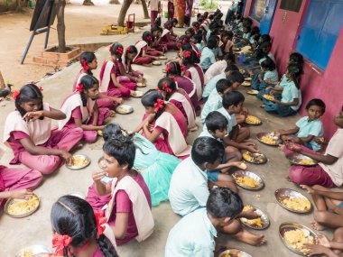 Puducherry, Tamil Nadu, Hindistan - Aralık yaklaşık, 2018. Bazı masala ile pirinç onların sağ eli ile yemek tanımlanamayan zavallı sınıf çocuk grubu ile açık havada, katta oturan üniformalar. Öğle yemeği zamanı, genel hükümet okulda sağlıksız gıda