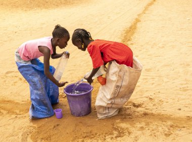 Bour, Senegal, Afrika, Aralık 2021 'de. Kimliği belirsiz Afrikalı çocuklar sokakta çuval yarışı yapıyor. Başlamak için havuzu suyla doldurmaları gerekiyor. Takım sporu çok komik.