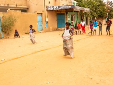 Bour, Senegal, Afrika, Aralık 2021 'de. Kimliği belirsiz Afrikalı çocuklar sokakta çuval yarışı yapıyor. Başlamak için havuzu suyla doldurmaları gerekiyor. Takım sporu çok komik.