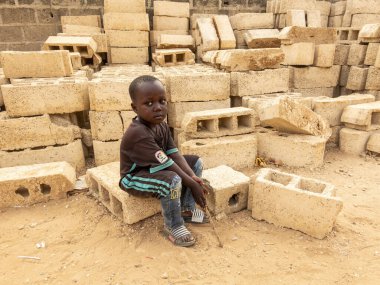 Bour, Senegal, Afrika, Aralık 2021 'de. Kimliği belirsiz Afrikalı bir çocuk sokakta oturuyor, üzgün ve fakir görünüyor. Afrika 'da yoksulluk ve çocuk için okula gitme zorluğu