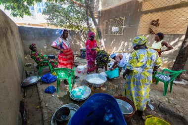 Bour, Senegal - Aralık 2021 civarı. Geleneksel renkte giyinmiş, tanımlanamayan kadınlar açık mutfakta temel gıdalarla yemek pişiriyorlar ama harika yemekler yapıyorlar. Afrika 'da yoksulluk