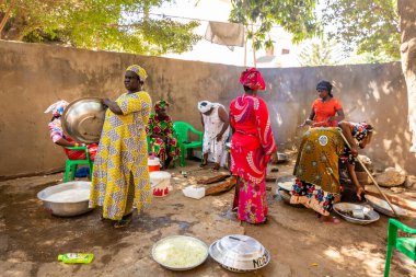 Bour, Senegal - Aralık 2021 civarı. Geleneksel renkte giyinmiş, tanımlanamayan kadınlar açık mutfakta temel gıdalarla yemek pişiriyorlar ama harika yemekler yapıyorlar. Afrika 'da yoksulluk