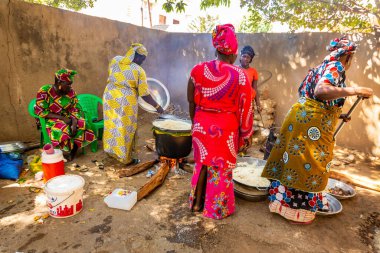 Bour, Senegal - Aralık 2021 civarı. Geleneksel renkte giyinmiş, tanımlanamayan kadınlar açık mutfakta temel gıdalarla yemek pişiriyorlar ama harika yemekler yapıyorlar. Afrika 'da yoksulluk