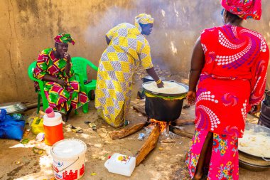 Bour, Senegal - Aralık 2021 civarı. Geleneksel renkte giyinmiş, tanımlanamayan kadınlar açık mutfakta temel gıdalarla yemek pişiriyorlar ama harika yemekler yapıyorlar. Afrika 'da yoksulluk