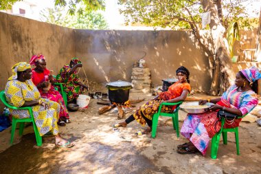 Bour, Senegal - Aralık 2021 civarı. Geleneksel renkte giyinmiş, tanımlanamayan kadınlar açık mutfakta temel gıdalarla yemek pişiriyorlar ama harika yemekler yapıyorlar. Afrika 'da yoksulluk