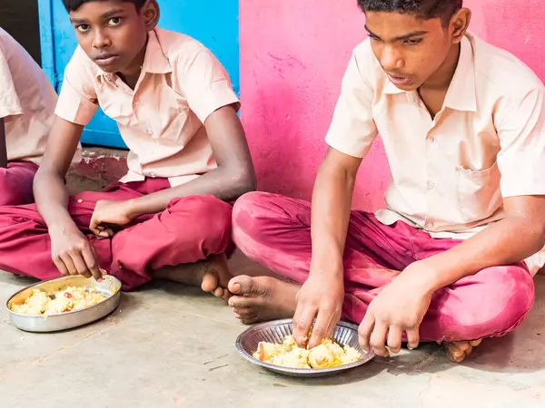 Puducherry, Tamil Nadu, Hindistan - Aralık yaklaşık, 2018. Bazı masala ile pirinç onların sağ eli ile yemek iki kimliği belirsiz zavallı sınıf çocuklar yere dış üzerinde oturan üniformalar. Öğle yemeği zamanı, genel hükümet okulda sağlıksız gıda