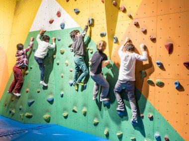 Bilim Merkezi, Paris, Fransa - Kasım 2019. Kimliği belirsiz genç sporcu kadınlar ve okul çocuğu ellerinde küçük kayalarla renkli duvara tırmanıyorlar.