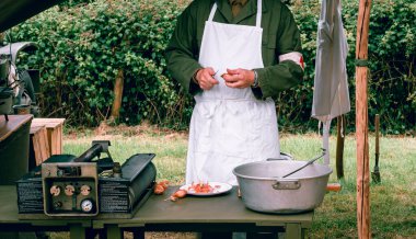 SAINTE MERE L'EGLISE, NORMANDY, FRANCE - JUNE 6 2023. Second world war commemoration. Military camp reconstitution Authentic scene of unidentified army cooker with table tools onions. clipart