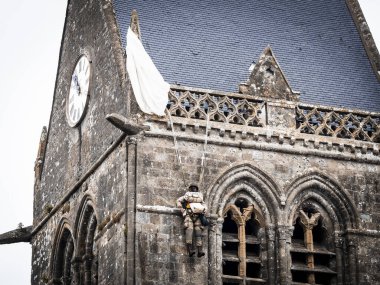 Aziz Michael L 'Eglise, Normandiya, Fransa - 6 Haziran 2023. İkinci Dünya Savaşı anısına. Askeri kamp yeniden yapılandırıldı. Kimliği belirsiz sahte asker makineli tüfek ve paraşütle sallanan çan kulesi kilisesi.