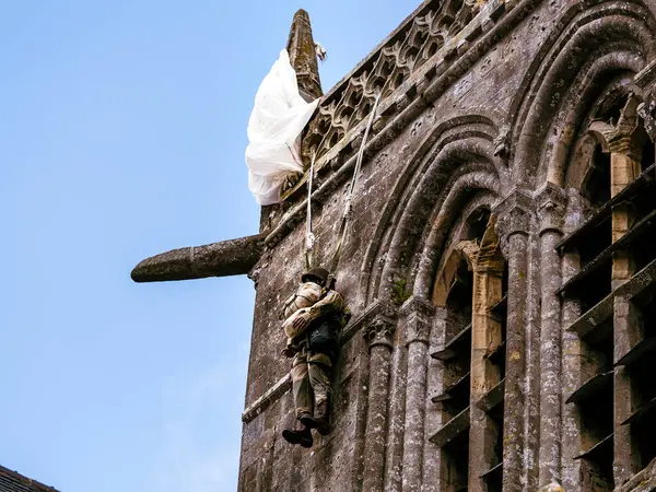 stock image SAINTE MERE L'EGLISE, NORMANDY, FRANCE - JUNE 6 2023. Second world war commemoration. Military camp reconstitution. Unidentified armed fake soldier with machine gun and parachute hanged bell tower church