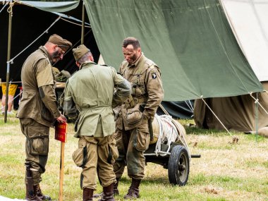 SAINTE MERE L'EGLISE, NORMANDY, FRANCE - JUNE 6 2023. Second world war commemoration. Military camp reconstitution Unidentified soldiers people next to tents, military american war vehicles. clipart