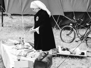 SAINTE MERE L'EGLISE, NORMANDY, FRANCE - JUNE 6 2023. Second world war commemoration. Military camp reconstitution Unidentified nurse with medical equipments next to military tent clipart