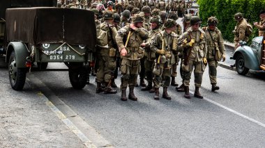 SAINTE MERE L'EGLISE, NORMANDY, FRANCE - JUNE 6 2023. Second world war commemoration. Military camp reconstitution. Unidentified armed troop soldiers walking after liberation clipart