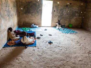 Bour, Senegal - CIRCA Mart 2021. Kimliği belirsiz Afro Afrikalı Senegalli ergen sünnet sonrası kum evinde oturuyor. Çok acı verici.