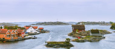 Rıhtım kenarındaki kırmızı ve beyaz kulübelerle rıhtım boyunca rıhtıma yanaşmış tekneler, Flekkeroya adasındaki deniz kenarındaki yazlık kulübeler. Kristiansand, Norveç