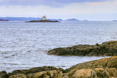 The Katland Lighthouse stands on a small rocky island, surrounded by the sea, with distant hills in the background. Flekkefjord, Norway clipart