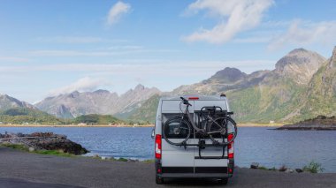 Lofoten 'da fiyort kenarında bisikleti olan bir karavan, macera yolculuğu için mükemmel. Göz kamaştırıcı dağ manzarası ve berrak gökyüzü güzel bir manzara yaratır. Lofoten Adaları, Norveç