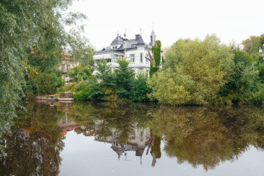 Şehir parkındaki yemyeşil ve nehir kenarındaki villa Svartan Nehri 'nde uzun ağaçlar ve yansımalarla dolu. Rahatlama ve kentsel kaçış kavramı. Orebro, İsveç. Metin için boşluk