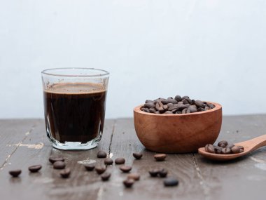 Cam bardakta siyah espresso kahvesi ve ahşap bir masada kahve çekirdekleri.