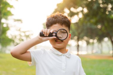 image of asian boy using magnifying glass in park