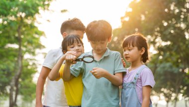 image of asian kids using magnifying glass in park